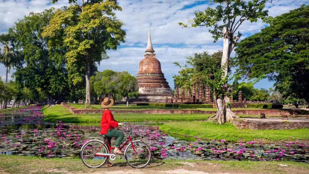 Woman riding bicycle looking at old Buddhist temple in Sukhothai historical park